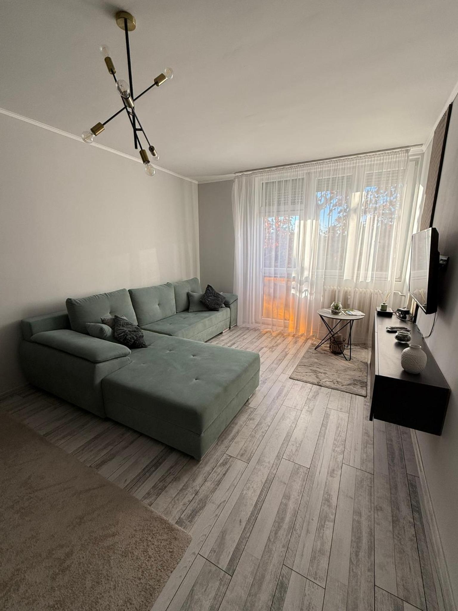 Boulevard Apartman – Nappali zöld sarokkanapéval és nagy ablakkal